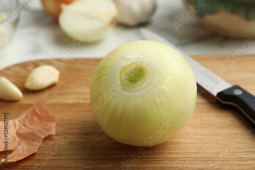 Peeled onion and knife on wooden board  closeup