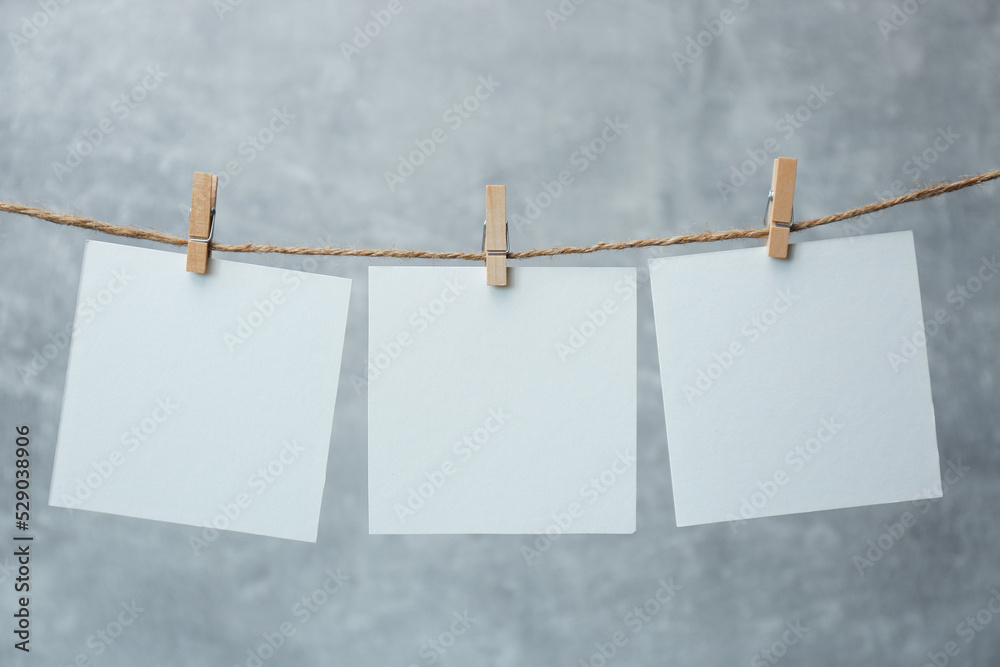 Wooden clothespins with blank notepapers on twine against grey background. Space for text Wooden clothespins with blank notepapers on twine against grey background. Space for text