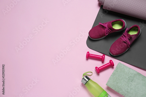 Exercise mat, dumbbells, shoes, towel and bottle of water on pink background, flat lay. Space for text