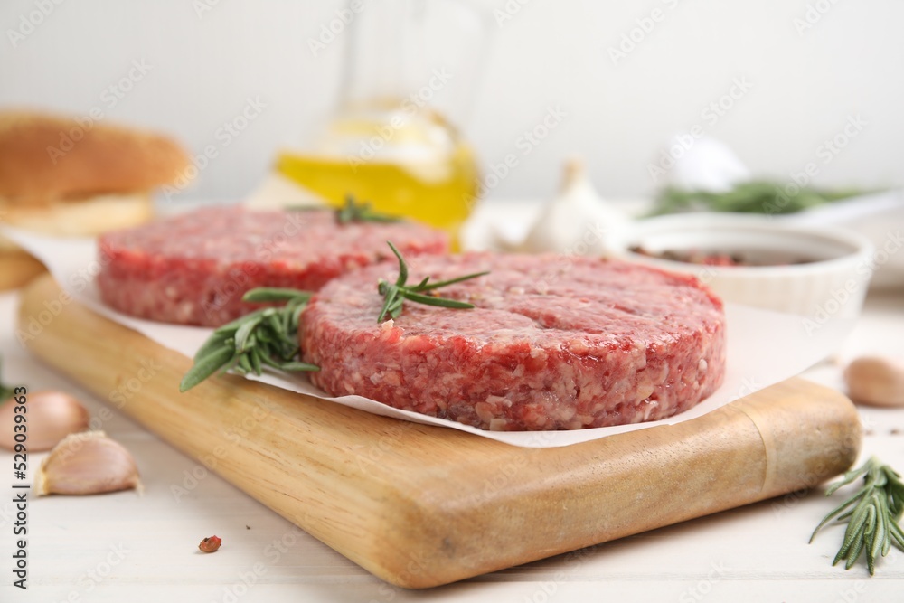 Raw hamburger patties with rosemary on white wooden table, closeup