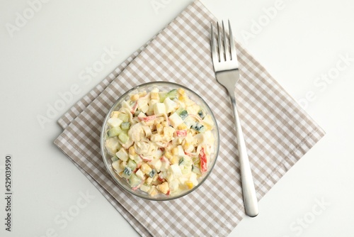 Delicious salad with fresh crab sticks in glass bowl on white table, top view