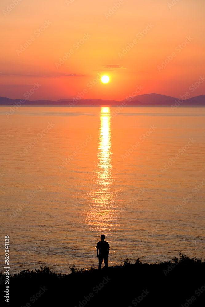 The silhouette of a man standing on the seashore during sunrise.