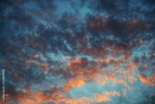 Himmellandschaft mit dunkelblauem und orangenem Wolkengebilde bei Sonnenuntergang am Abend im Sommer