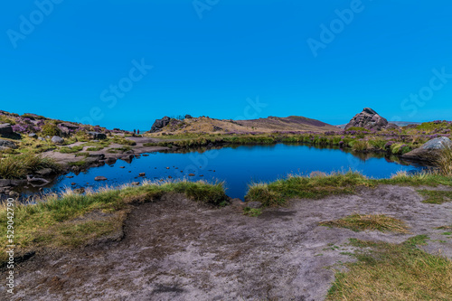 A view across Doxey Pool looking towards the cliff edge on the summit of the Roaches escarpment, Staffordshire, UK in summertime