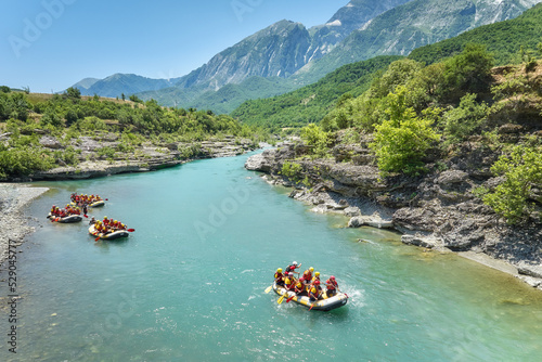 A group of four yellow rafts floating among the rocks on the crystal clear, blue-green water of Vjosa river, Albania.