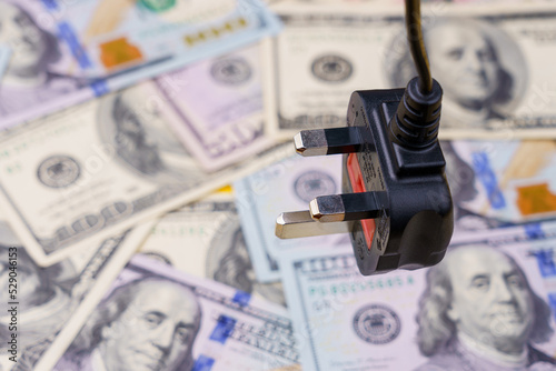 Electric cord plug and dollars on a blurred background, selective focus. The concept of the energy crisis