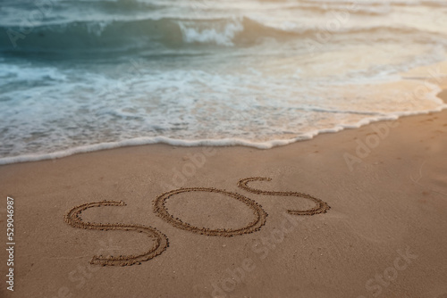 SOS message drawn on sandy beach near sea
