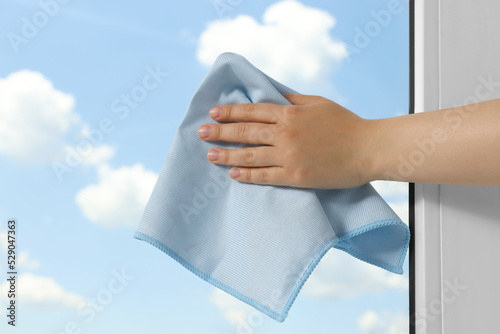 Woman cleaning window glass with rag indoors, closeup