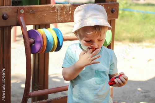 Defocused child with dirty hands. The boy put his finger with sand in his mouth. Copy space - the concept of active recreation on the playground in summer, entertainment, bacteria, children's hygiene