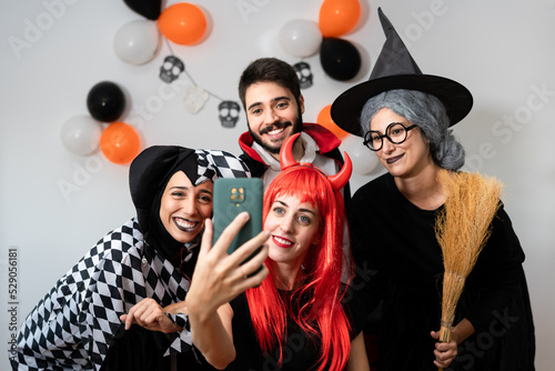 Halloween party at home. Devil, witch, dracula and harlequin posing taking a selfie with their smartphone