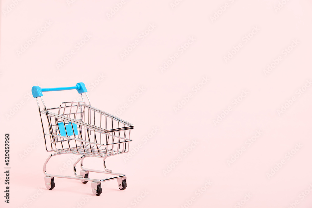 Empty shopping cart with light blue details on a pastel pink background. Minimalist design with copy space. Concepts: market deals, seasonal sales and discounts, black friday. Empty shopping cart with light blue details on a pastel pink background. Minimalist design with copy space. Concepts: market deals, seasonal sales and discounts, black friday.