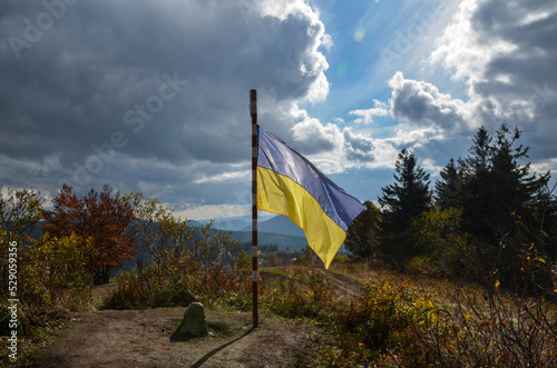 Ukrainian national flag waving on the wind surrounded autumn mountain landscape under blue sky with clouds
