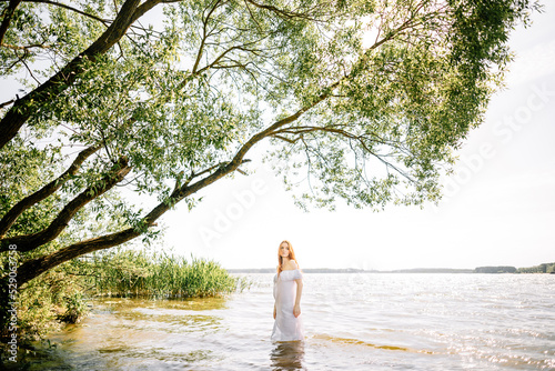 Woman in summer dress standing on seashore and looking at horizon. Young beautiful girl standing in water