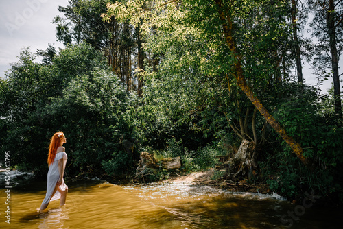 Woman in summer white dress stands on the seashore and looks at the horizon. Young beautiful girl standing in the water