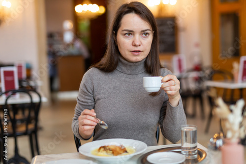 Canvas Print Brunette woman enjoying cup of aromatic espresso with delicious apple strudel during breakfast in cafe