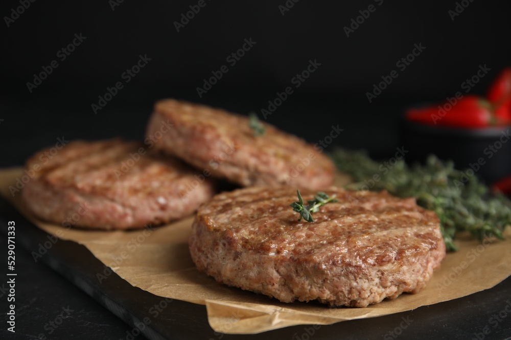 Tasty grilled hamburger patties with thyme on black table, closeup