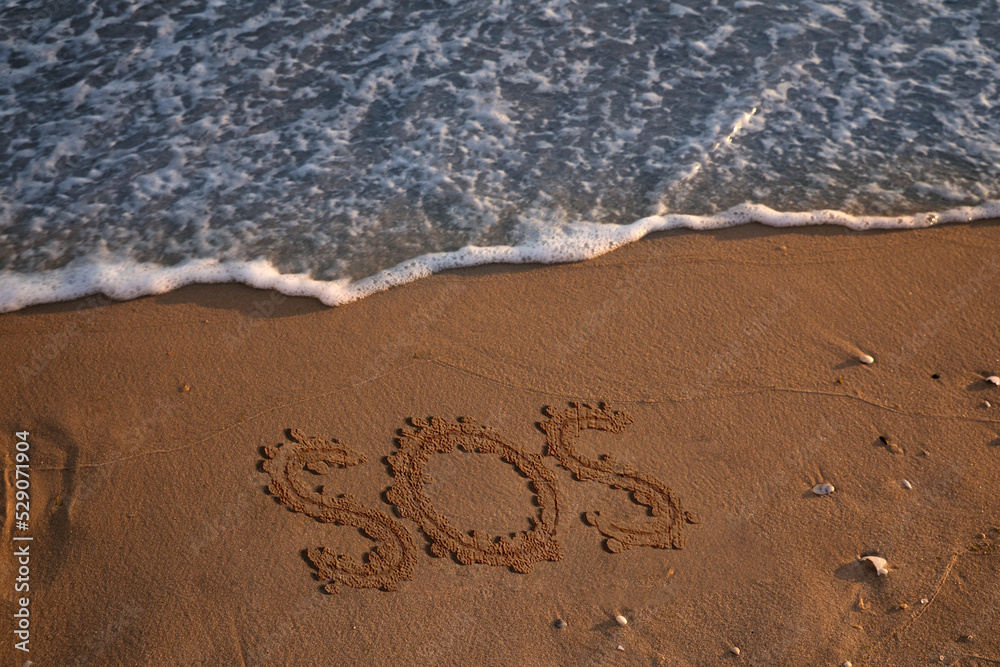 SOS message drawn on sandy beach near sea, above view SOS message drawn on sandy beach near sea, above view