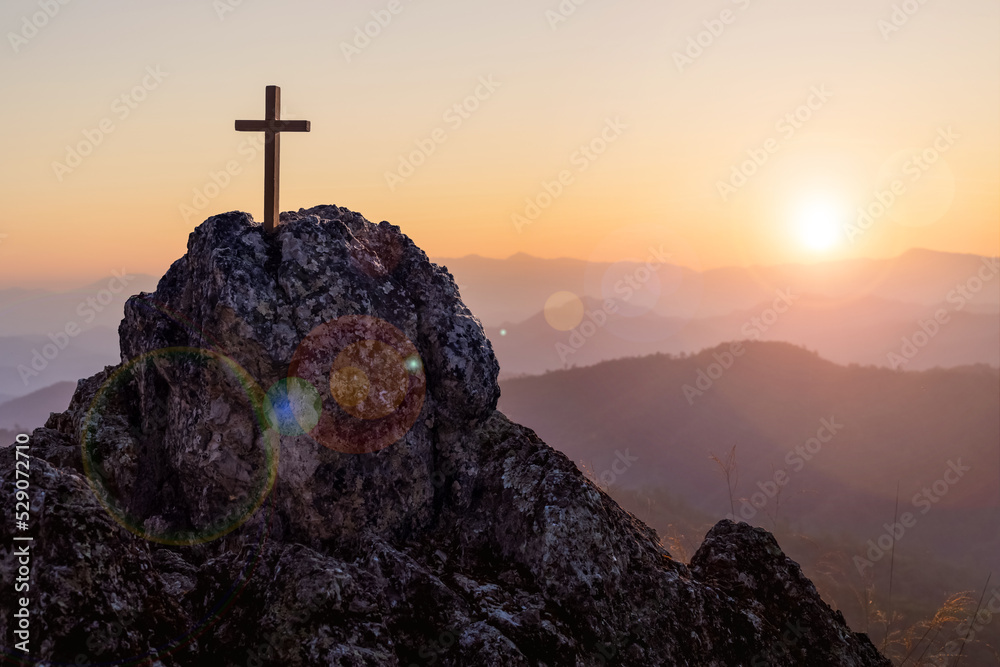 Silhouettes of crucifix symbol on top mountain with bright sunbeam on the colorful sky background