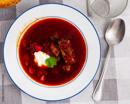 Homemade beetroot soup with vegetables and meat decorated by sour cream and parsley, traditional Ukrainian or Russian food
