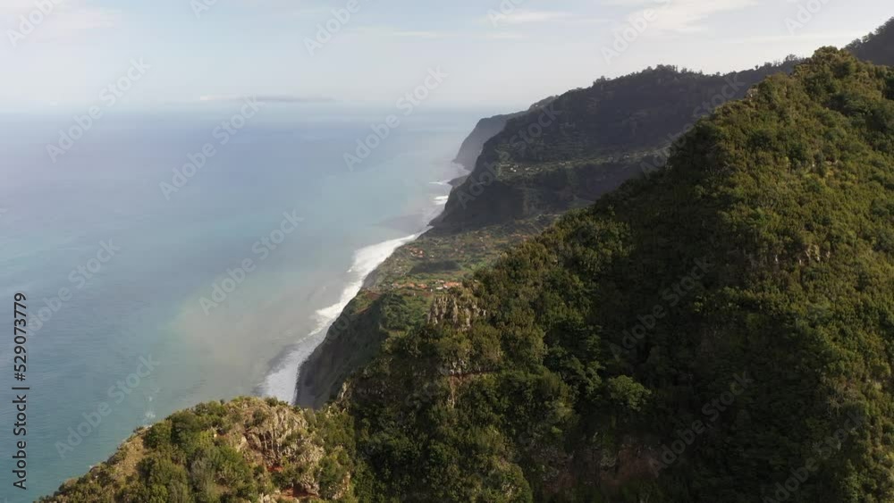Drone shot flying over a mountain top to reveal the landscape and valley below with a small village in Madeira. Drone shot flying over a mountain top to reveal the landscape and valley below with a small village in Madeira.