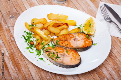 Grilled salmon steak served on plate with fried potato. Garnished fish ready-to-eat.