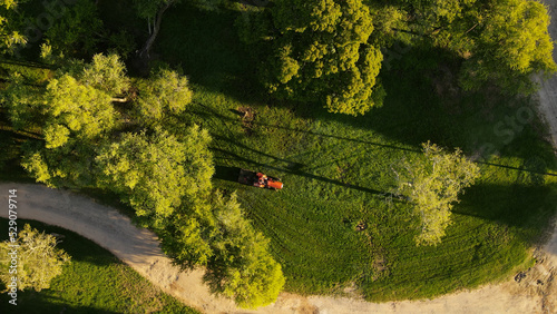 Aerial top-down circling over red tractor cutting green grass