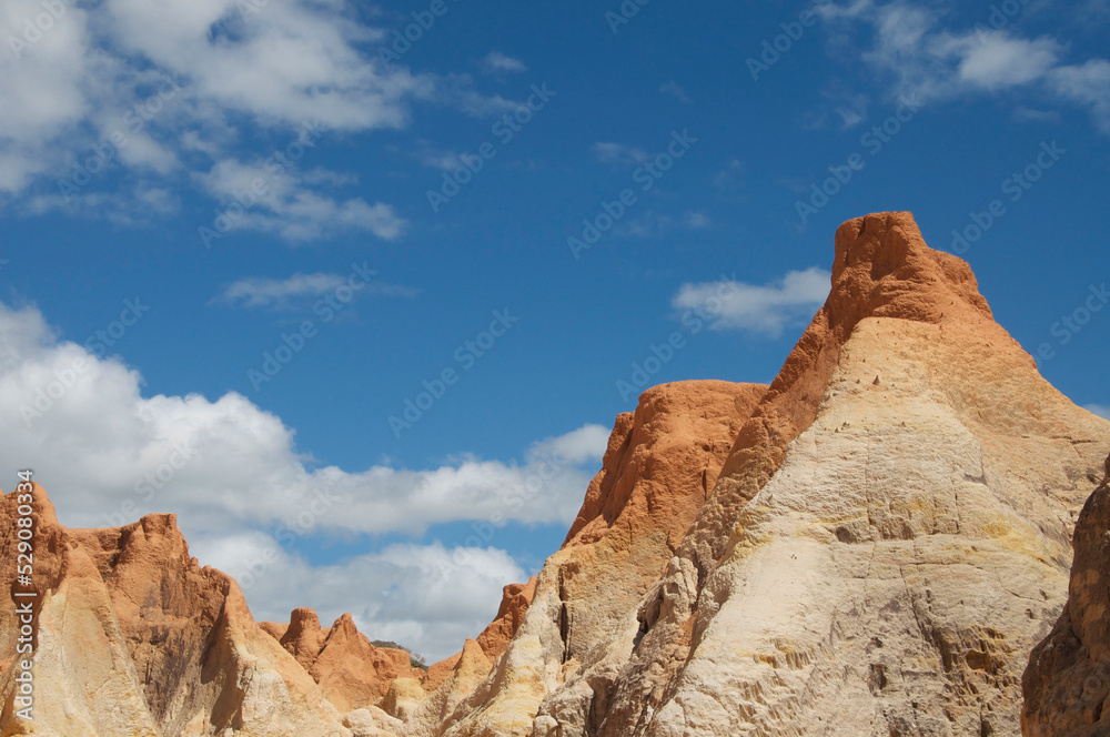 Crag of colored sand and white clouds in a blue sky.