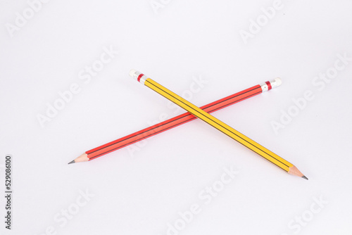 Yellow pencil placed on a red pencil on a white background.