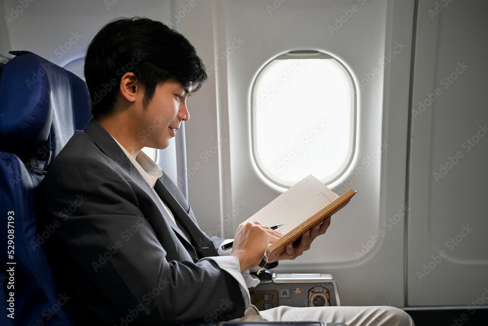 Handsome Asian businessman reading a book during the flight for his business trip.