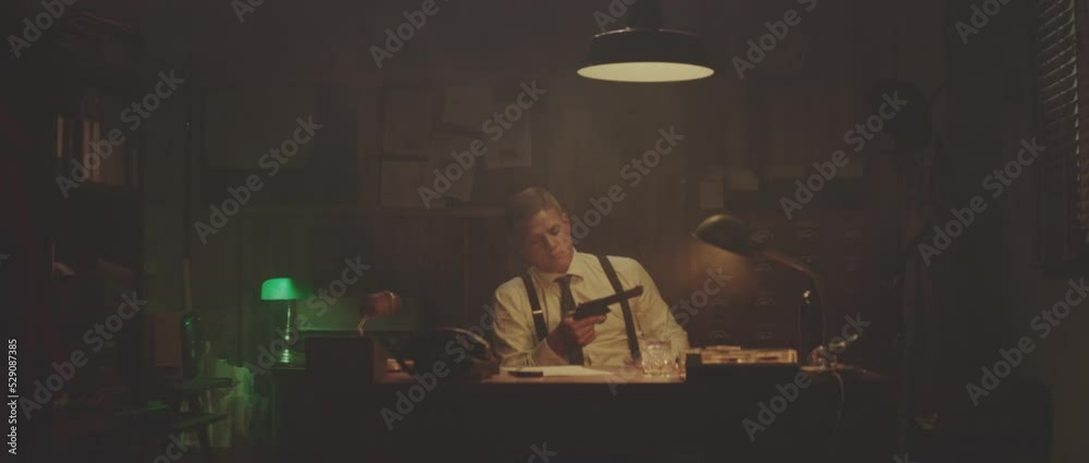 Caucasian man in shirt sitting in office in evening and holding revolver. Retro style detective using deduction for solving challenging cases. Caucasian man in shirt sitting in office in evening and holding revolver. Retro style detective using deduction for solving challenging cases.