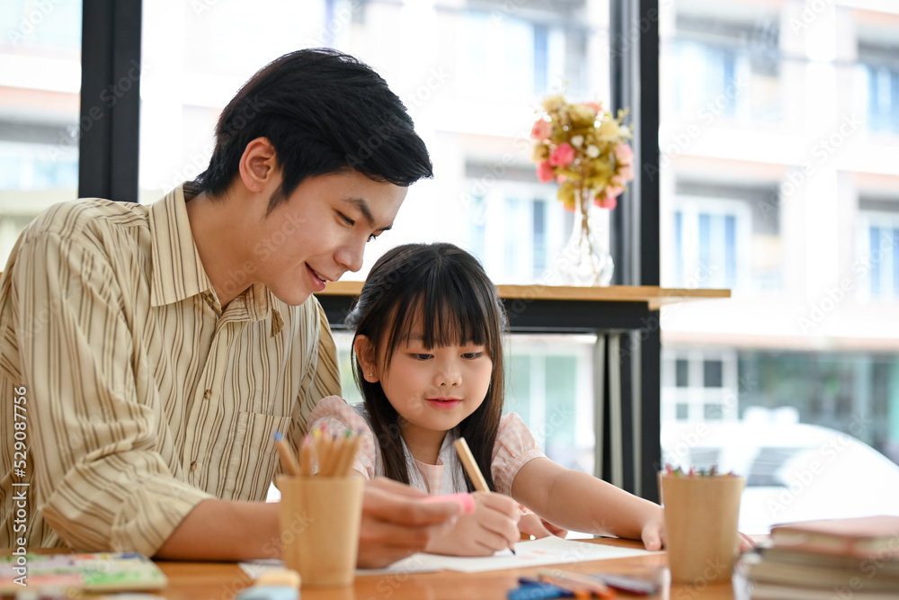 Cheerful Asian male art teacher is teaching to his young female student. Cheerful Asian male art teacher is teaching to his young female student.
