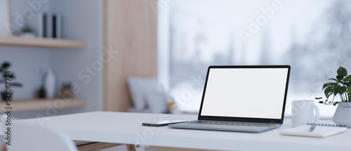Notebook laptop mockup and stuff on white tabletop over blurred modern home living room background © bongkarn