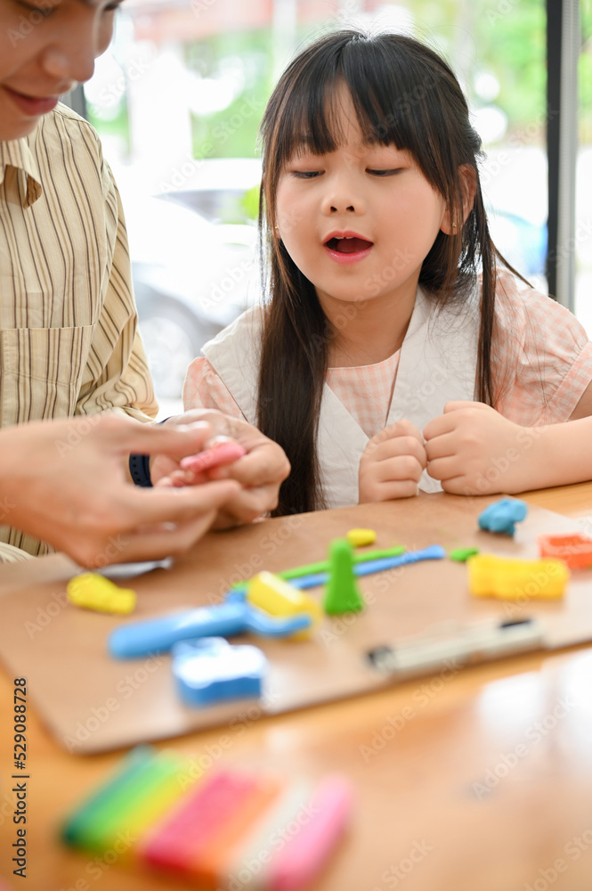 Charming young Asian girl enjoys playing play dough, moulding colorful clay with her brother