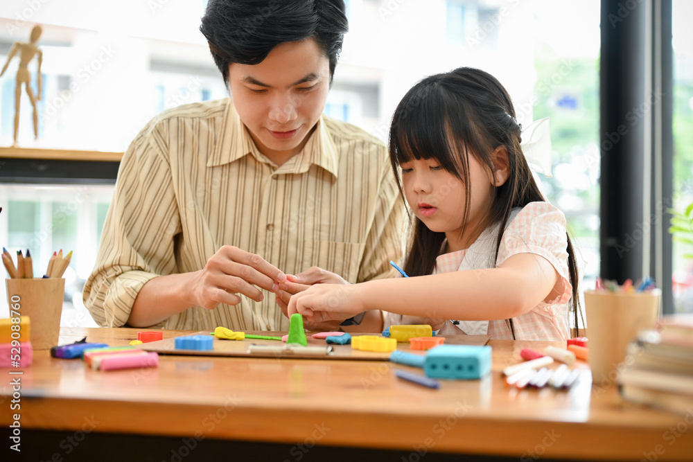Smiling Asian male art teacher and a young girl moulding colorful clay or plasticine together Smiling Asian male art teacher and a young girl moulding colorful clay or plasticine together