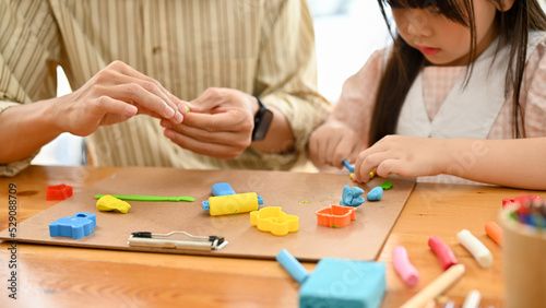 An adorable young Asian girl sculpting colorful clay, moulding clay with her dad. cropped image
