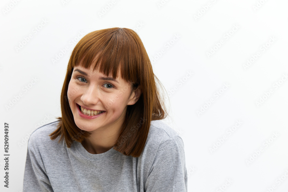 a happy, joyful, pleasant woman with red hair, smiling at the camera standing on a white background in a gray cotton T-shirt. Horizontal Studio Photography a happy, joyful, pleasant woman with red hair, smiling at the camera standing on a white background in a gray cotton T-shirt. Horizontal Studio Photography