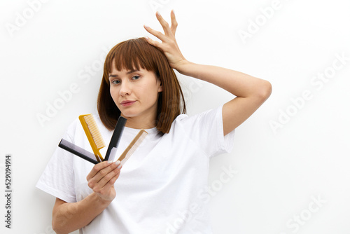 a beautiful  pleasant woman with a beautiful hairstyle holds her hand above her head in a funny gesture  and in another comb.