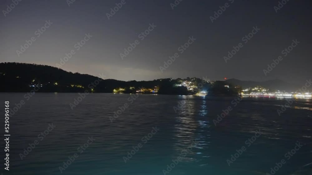 Night shot of a small docking area while going away from it on a small island next to a little village Night shot of a small docking area while going away from it on a small island next to a little village
