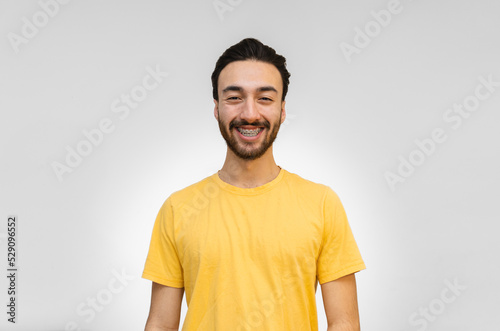 young latin man with braces smiling looking at camera, white background with yellow shirt