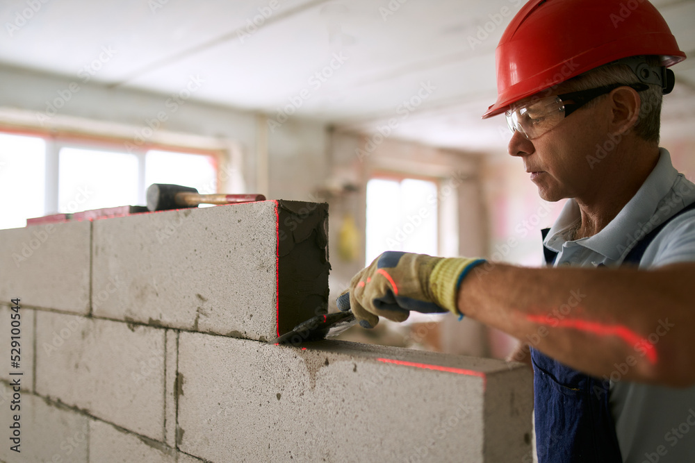 Bricklayer applies adhesive glue on autoclaved aerated concrete blocks with notched trowel. Brickwork worker contractor removes excess mortar from foam concrete doing masonry with laser level. Bricklayer applies adhesive glue on autoclaved aerated concrete blocks with notched trowel. Brickwork worker contractor removes excess mortar from foam concrete doing masonry with laser level.