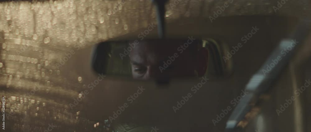 Inside car, male face in rear view mirror. Rainy evening. Retro style detective using deduction for solving challenging cases.