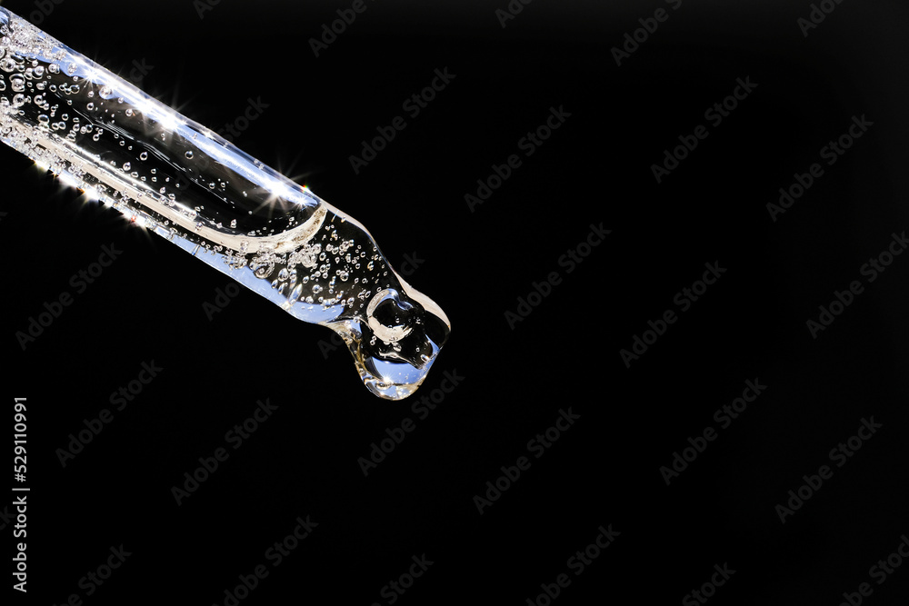 Transparent pipette with cosmetic liquid on a black background. Side view, close-up. Transparent pipette with cosmetic liquid on a black background. Side view, close-up.