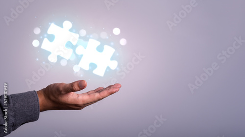Businessman holding a glowing white graphic jigsaw puzzle on technology blue background Find the right solution for the work job concept.