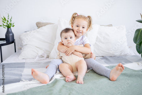 the older sister holds and hugs the baby at home on the bed, the love and friendship of the sisters in the family
