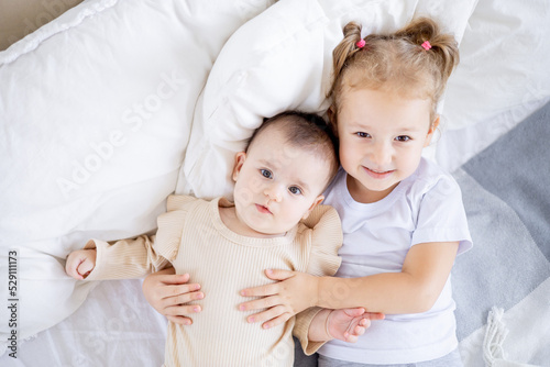 two sisters' children cuddle on the bed at home, the older sister holds the baby at home on the bed, the sisters' love and friendship in the family