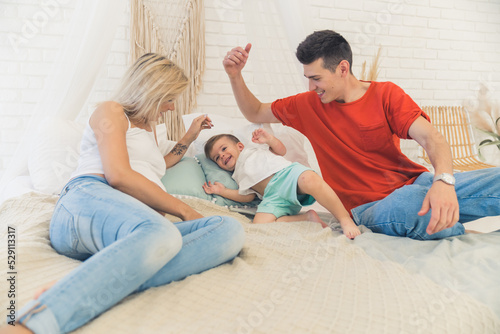 Quality leisure time with family. Two adult European married people lying on the bed and tickling their beloved four-year-old son. Casual clothing. High quality photo