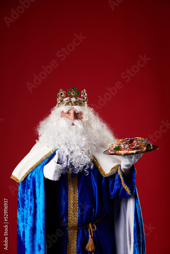 reyes magos holding a "roscón de reyes" in his hand on a red background