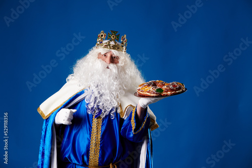 smiling king magician holding a "roscón de reyes" in his hand on a blue background