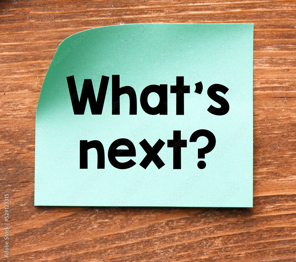 WHAT'S NEXT words on a small piece of paper and a wooden table. WHAT'S NEXT words on a small piece of paper and a wooden table.