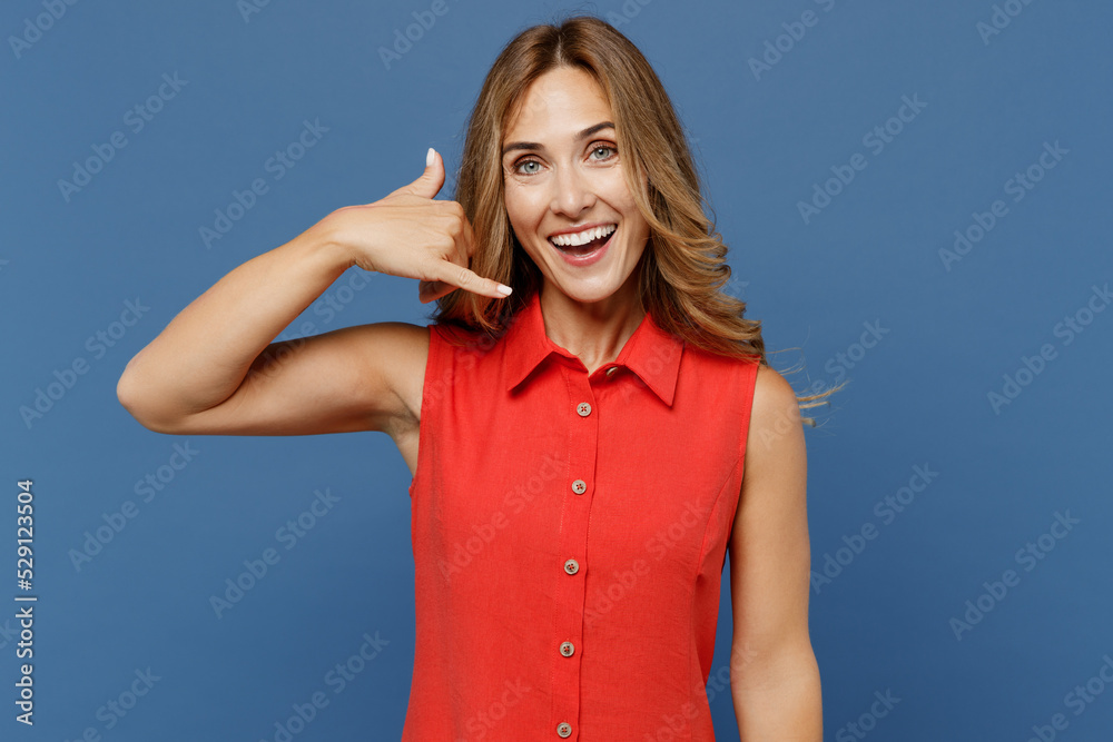 Young smiling happy fun caucasian woman 30s she wear red dress doing phone gesture like says call me back isolated on plain dark royal navy blue background studio portrait. People lifestyle concept.